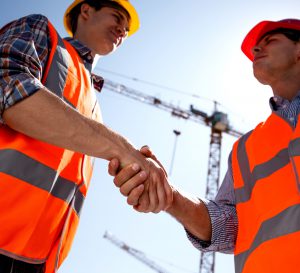 Structural engineer and architect dressed in orange work vests and  helmets shake hands on the building site near the crane . .